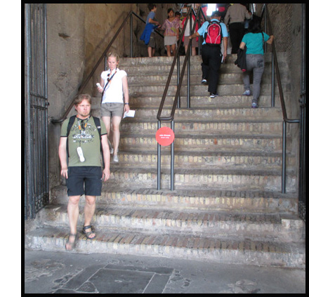 Photo shows a wide stone or marble stairway with a railing on each side and double railing in the middle.  All railings end on the 3rd step from the bottom.  A group of people are going up on the right half and two young women are coming down on the left - neither woman is using the railing.